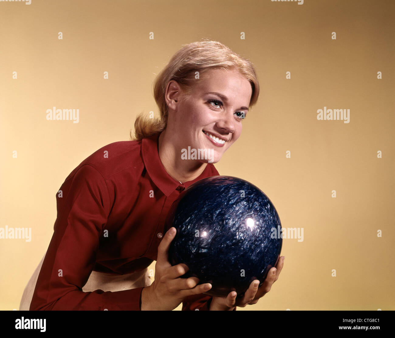 1960s YOUNG SMILING BLONDE WOMAN HOLDING BOWLING BALL WEARING RED SHIRT ABOUT TO BOWL Stock Photo