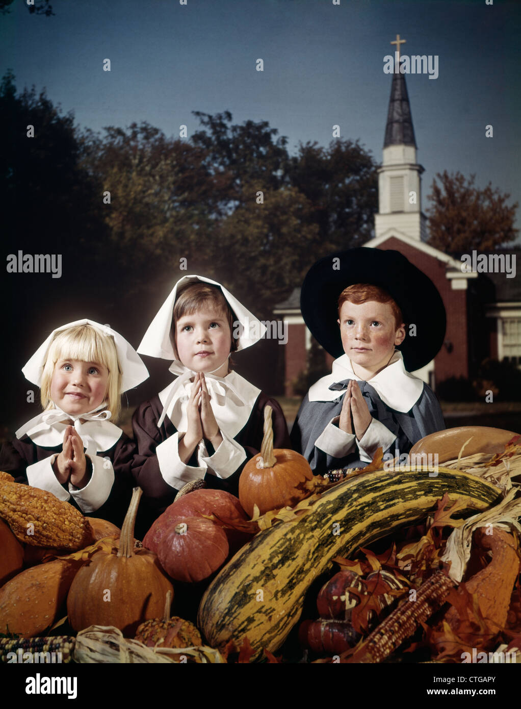 1970s THREE CHILDREN WEARING PILGRIM COSSTUMES SAYING GRACE BEFORE THANKSGIVING Stock Photo