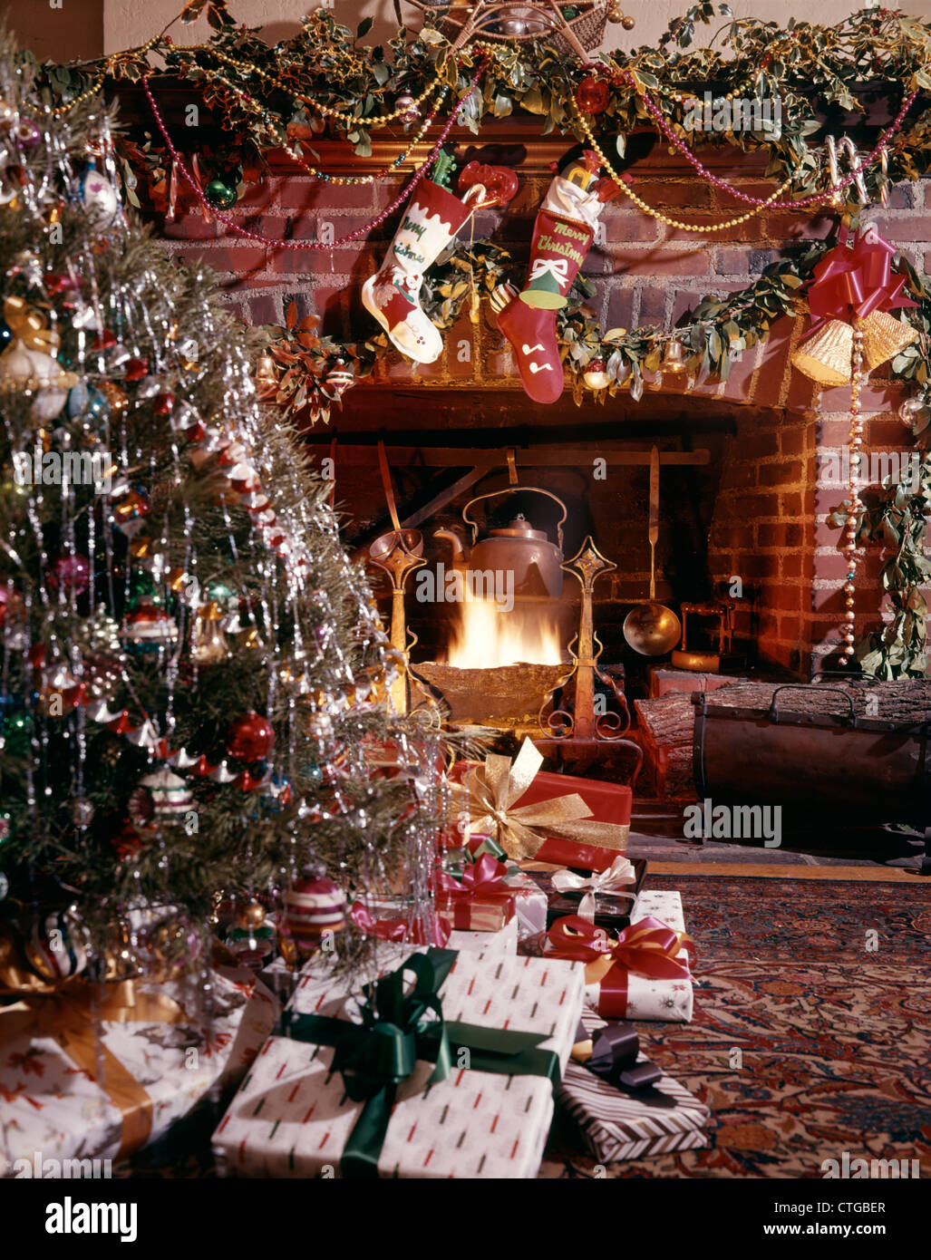 1960s CHRISTMAS TREE STOCKINGS PRESENTS DECORATION AROUND BLAZING FIREPLACE Stock Photo