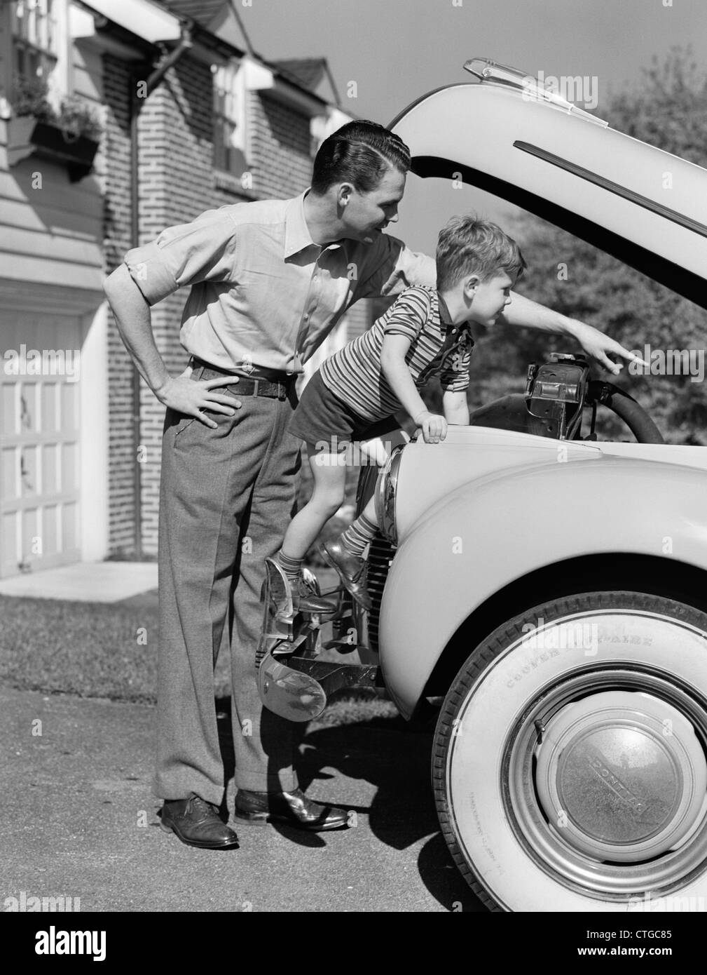1940s FATHER & SON CHECKING UNDER HOOD OF CAR IN DRIVEWAY Stock Photo