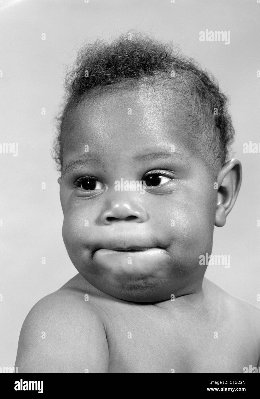 1960s PORTRAIT OF AFRICAN-AMERICAN BABY MAKING A FUNNY FACE BITING HIS LIP Stock Photo