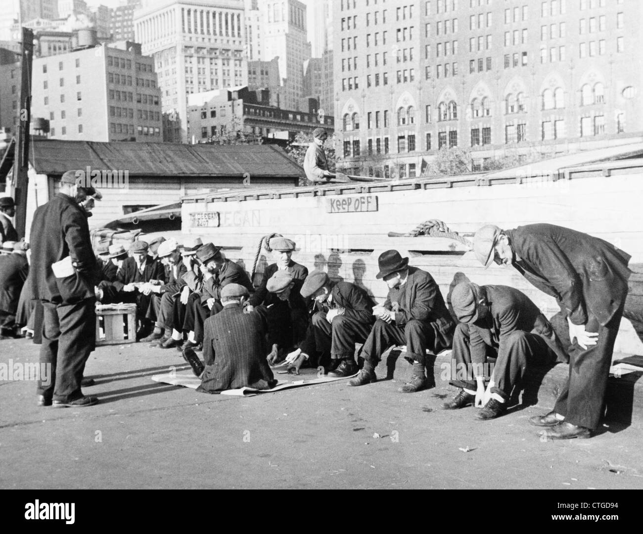 1930s UNEMPLOYED MEN SITTIN IN SUNSHINE ON COENTIES SLIP DOCK LOWER MANHATTAN NEW YORK CITY Stock Photo