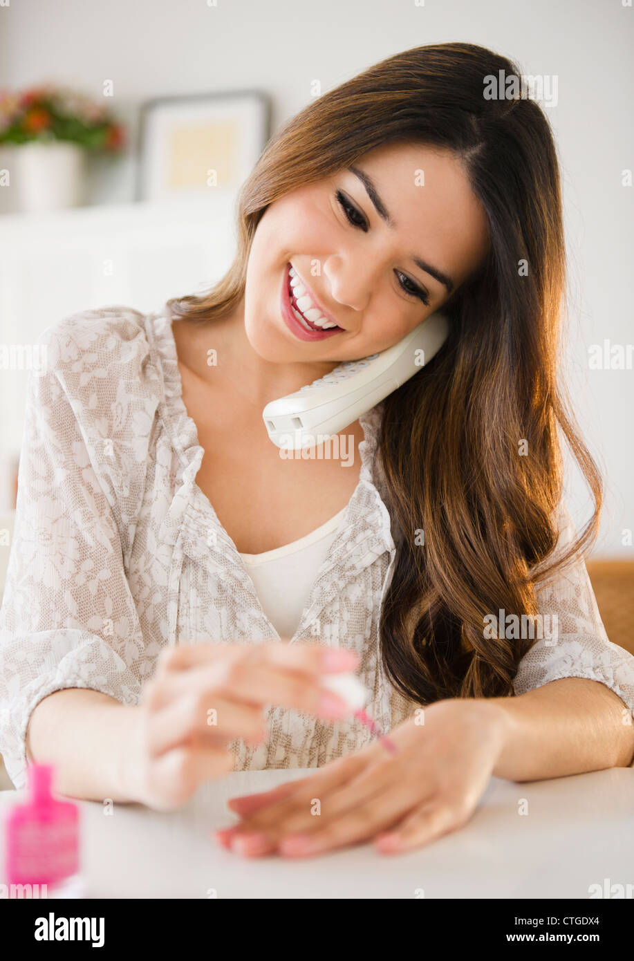 Hispanic woman talking on phone and painting fingernails Stock Photo