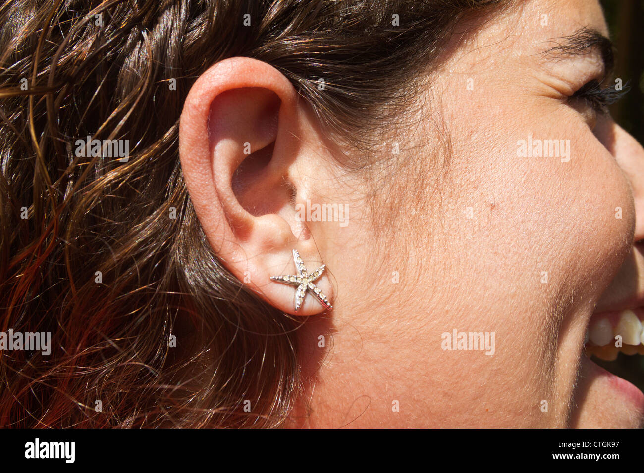 Star shaped earring on smiling young woman's ear. Stock Photo