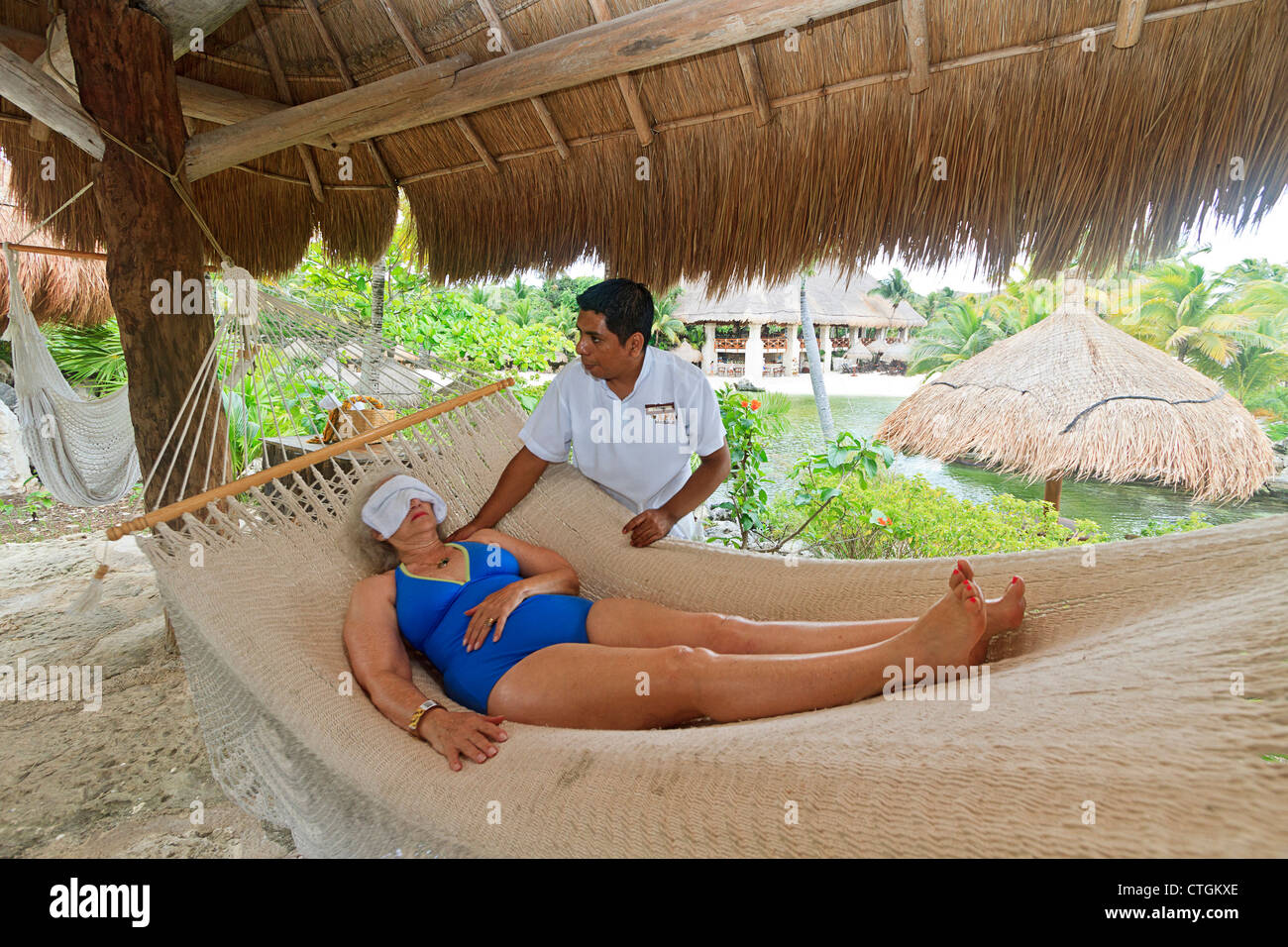 Woman enjoys massage from Maya man while lying in a hammock at Xcaret, an amusement park in Riviera Maya, Yucatan, Mexico. Stock Photo