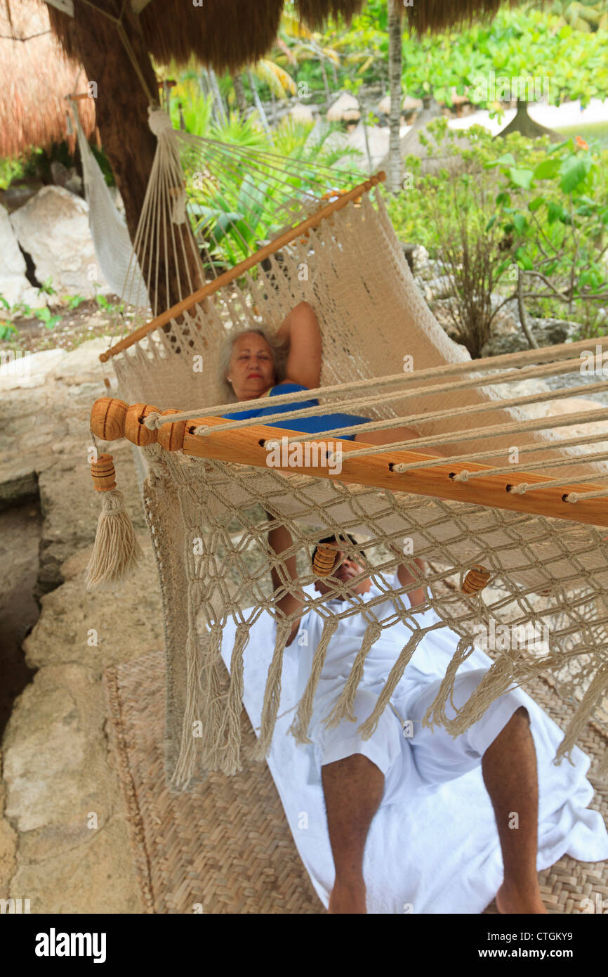 Woman enjoys massage from Maya man while lying in a hammock at Xcaret, an amusement park in Riviera Maya, Yucatan, Mexico. Stock Photo