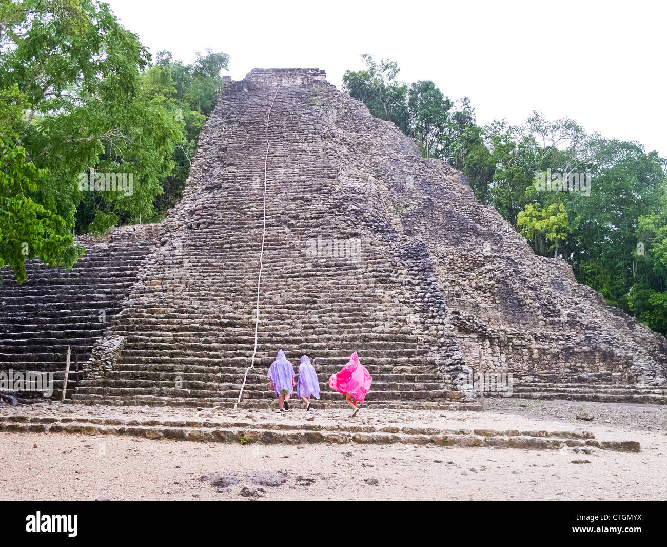 Visitors in raincoats climb Nohoch Muul, a Maya temple at Coba, Mexico Stock Photo