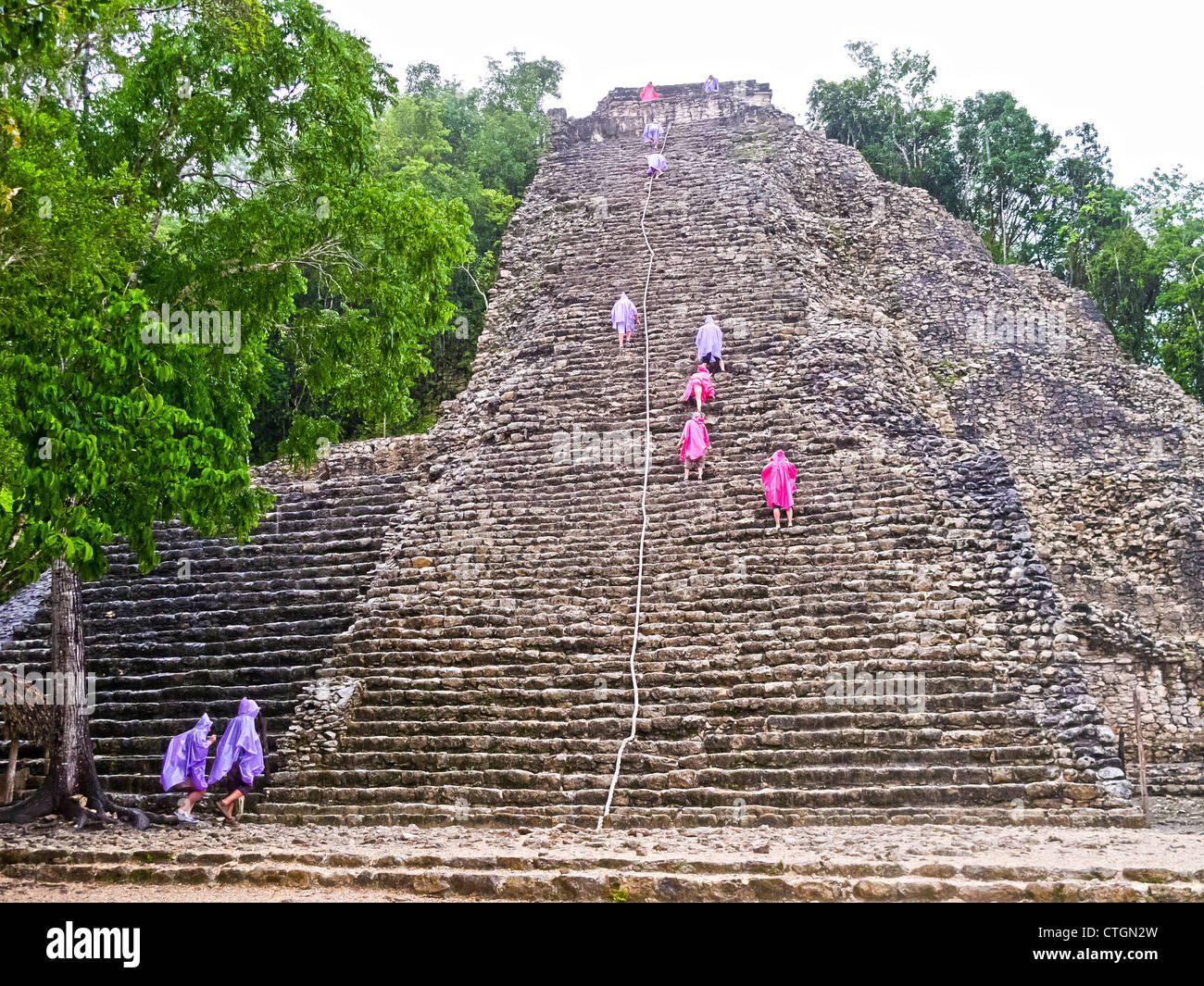 Visitors in raincoats climb Nohoch Muul, a Maya temple at Coba, Mexico Stock Photo