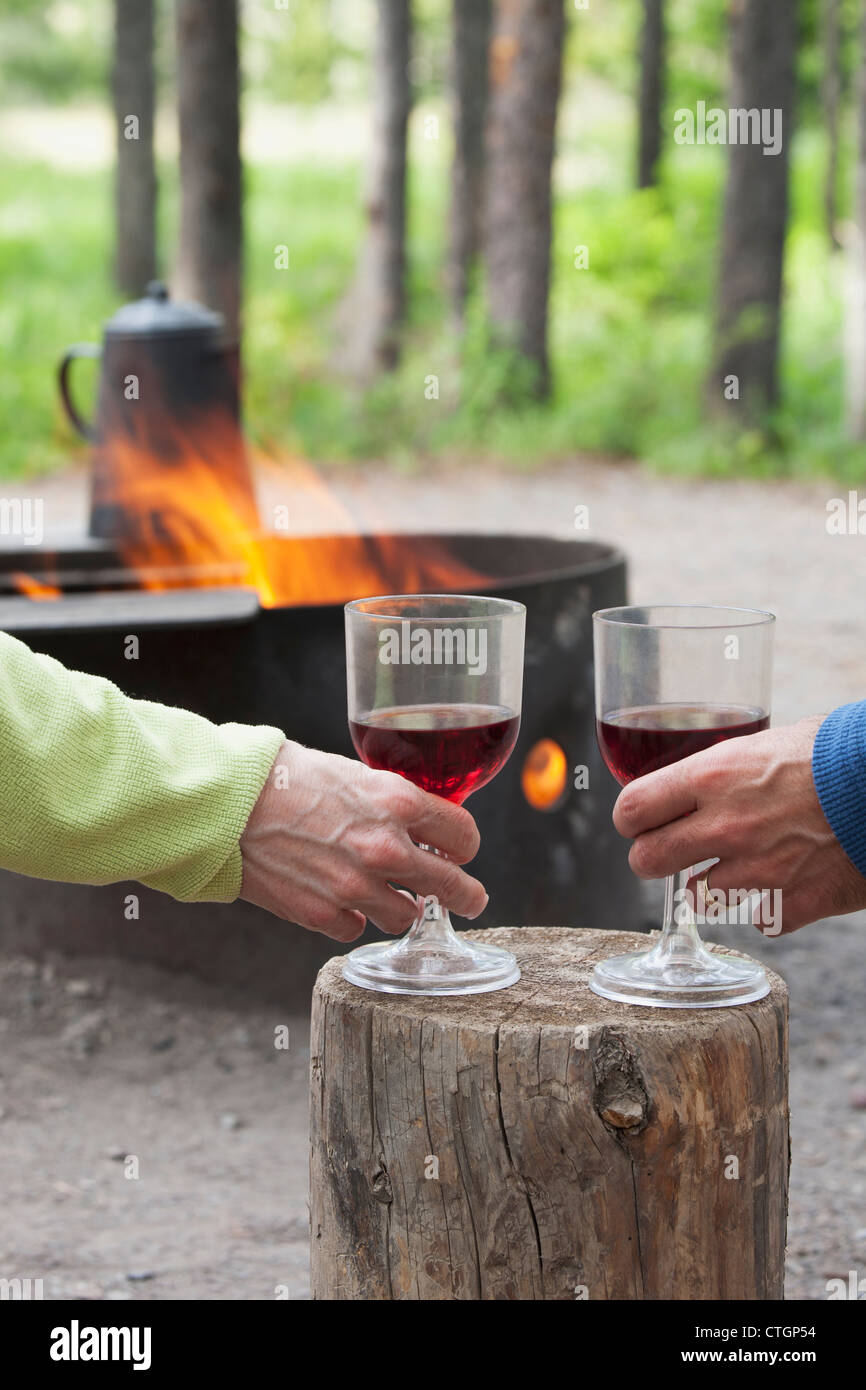 A Couple Holding Wine Glasses On A Block Of Wood With A Fire Pit