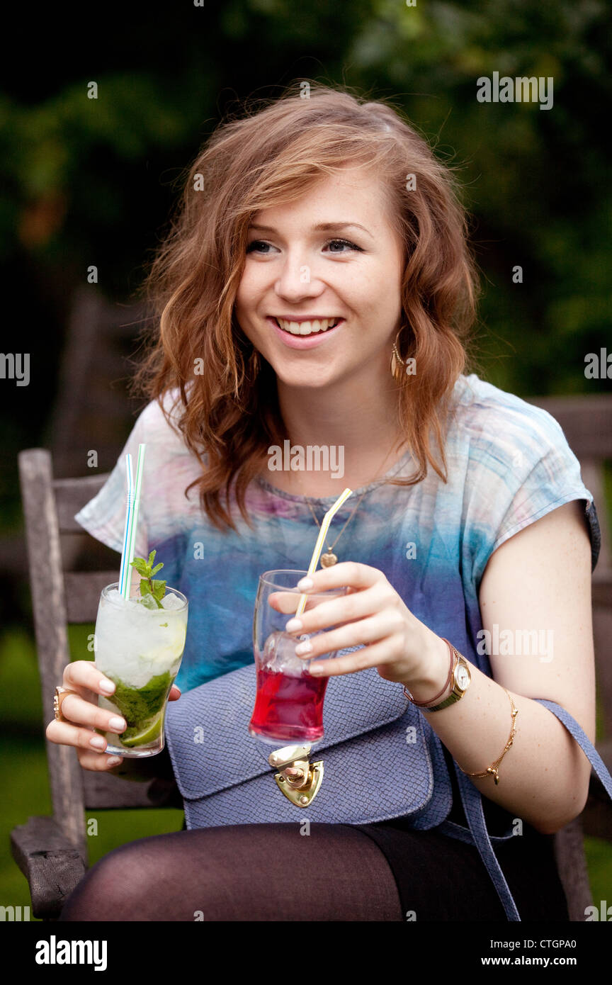 Attractive young caucasian woman holding two cocktails at a party, UK Stock Photo