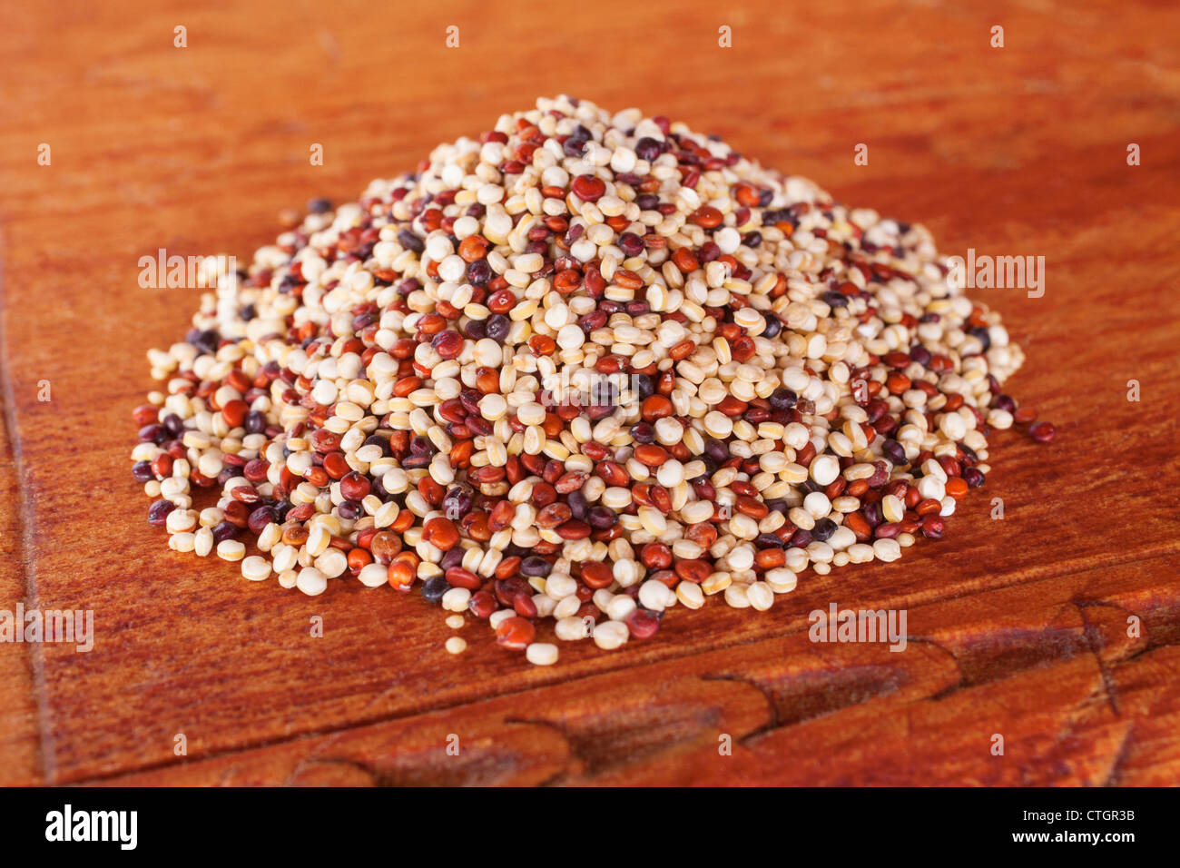 Ancient grains quinoa and amaranth in a pile on a wooden board. Quinoa contains white, red and black grains. Stock Photo