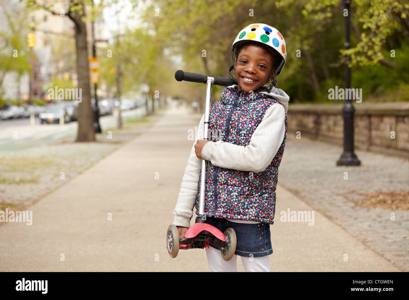 Mixed race girl holding push scooter on sidewalk Stock Photo