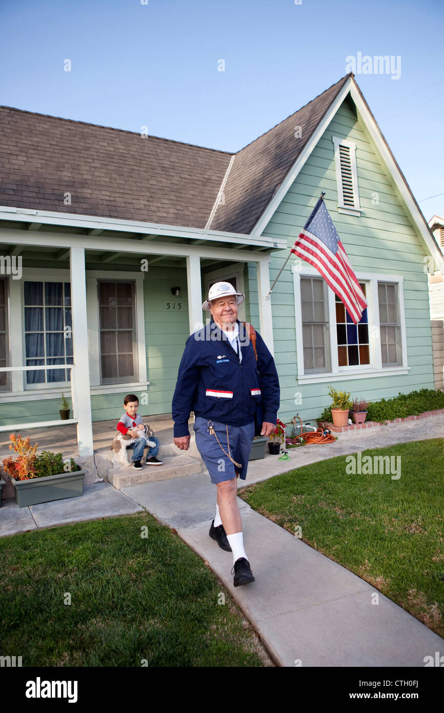 Caucasian mailman walking in front yard Stock Photo