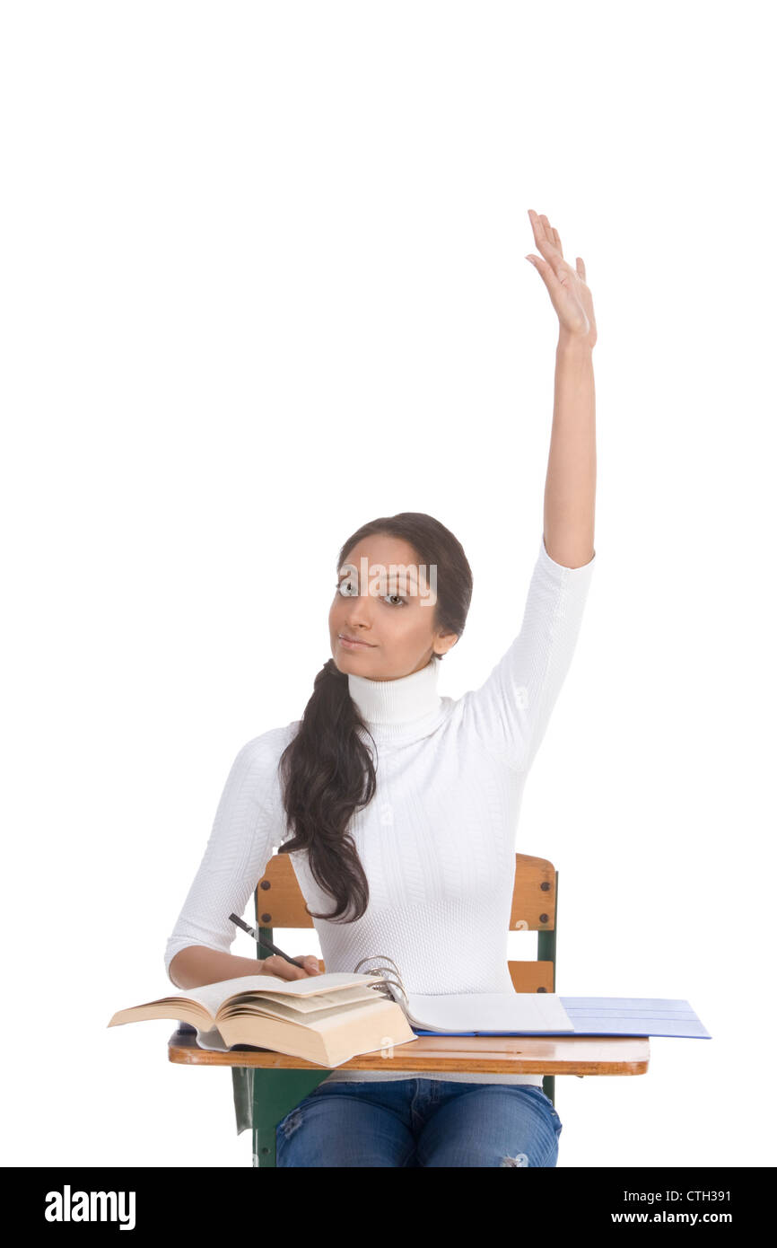 High school or college female student sitting by the desk raising her arm signaling that she know and is ready to answer Stock Photo