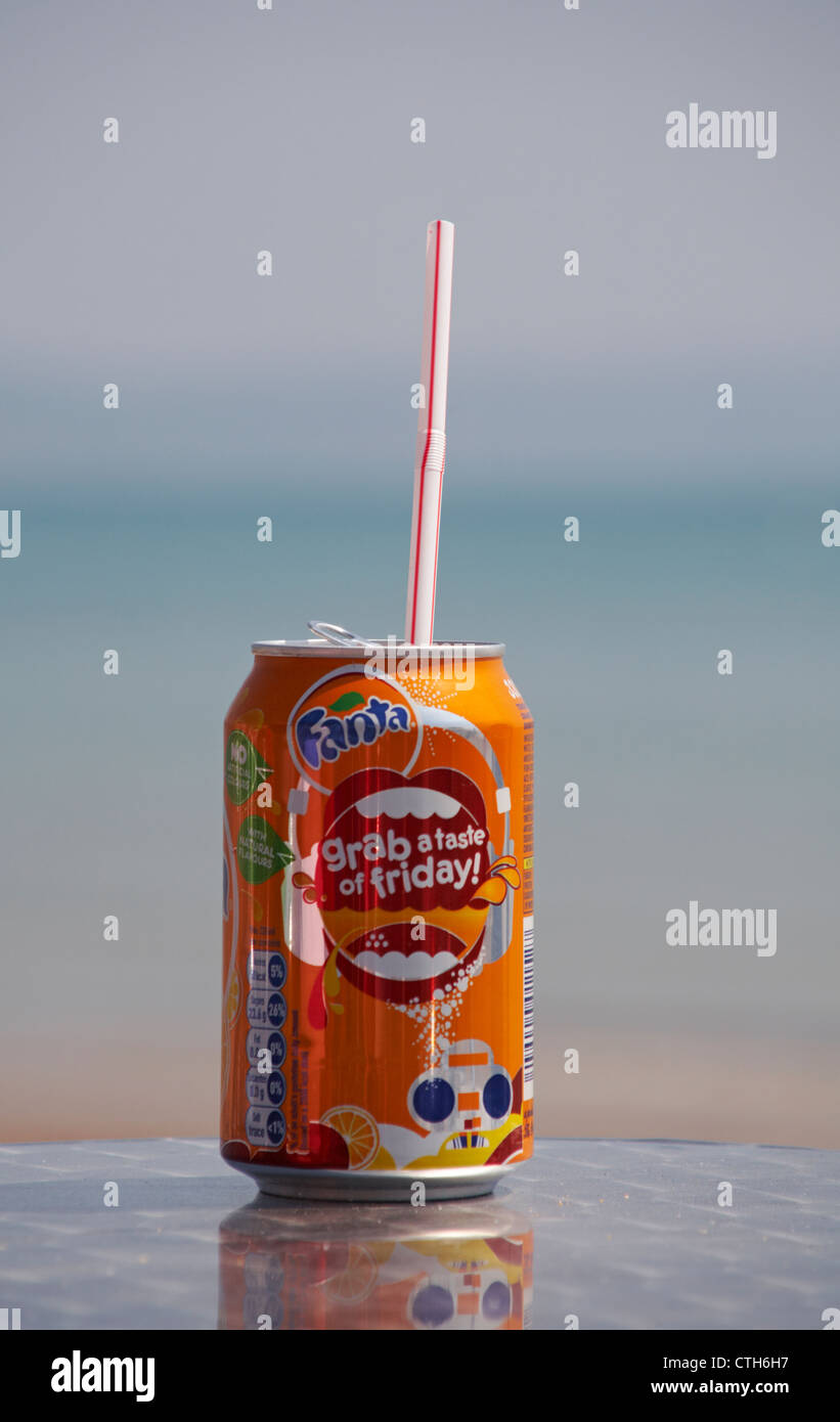 Enjoying a can of Fanta orange drink by the seaside at Weymouth, Dorset UK in May - drinks can with plastic straw Stock Photo