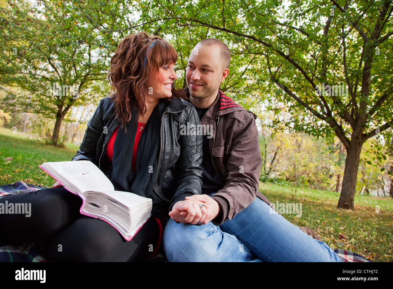 Couple Reading Bible Together In The Park; Edmonton, Alberta, Canada Stock Photo