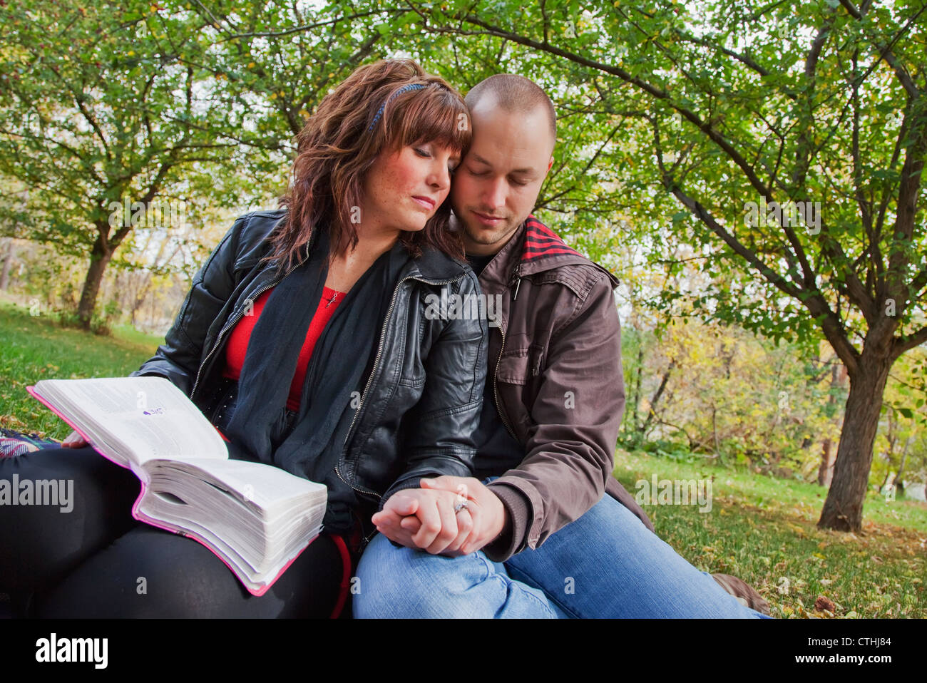 Couple Reading Bible And Praying Together In The Park; Edmonton, Alberta, Canada Stock Photo