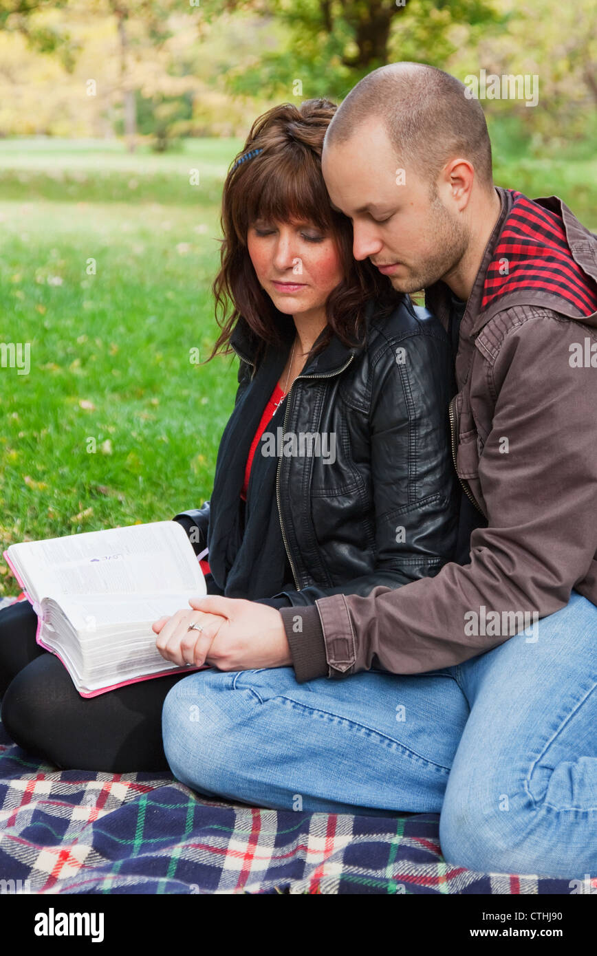 Couple Reading Bible And Praying Together In The Park; Edmonton, Alberta, Canada Stock Photo