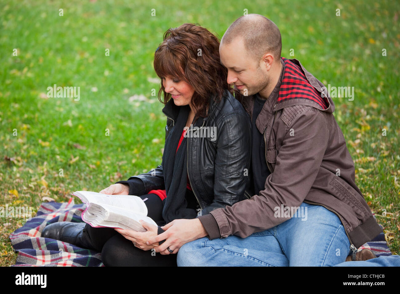 Couple Reading Bible Together In The Park; Edmonton, Alberta, Canada Stock Photo