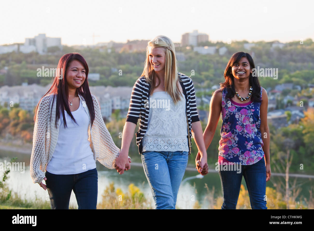Friends Walking In A City Park With The City Skyline In The Background; Edmonton, Alberta, Canada Stock Photo