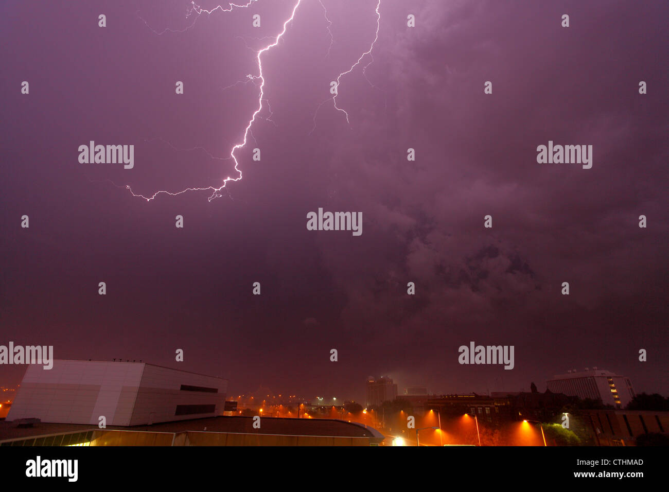 Lightning illuminates the sky purple during a thunderstorm over a city, accompanied by heavy rain and haze (visible in lower). Stock Photo
