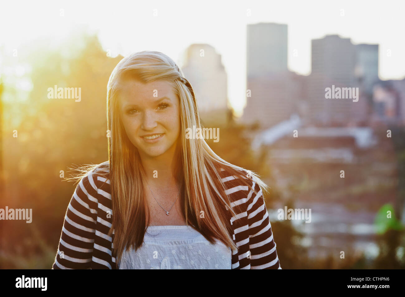 Portrait Of A Young Woman In A Park With The City Skyline In The Background; Edmonton, Alberta, Canada Stock Photo