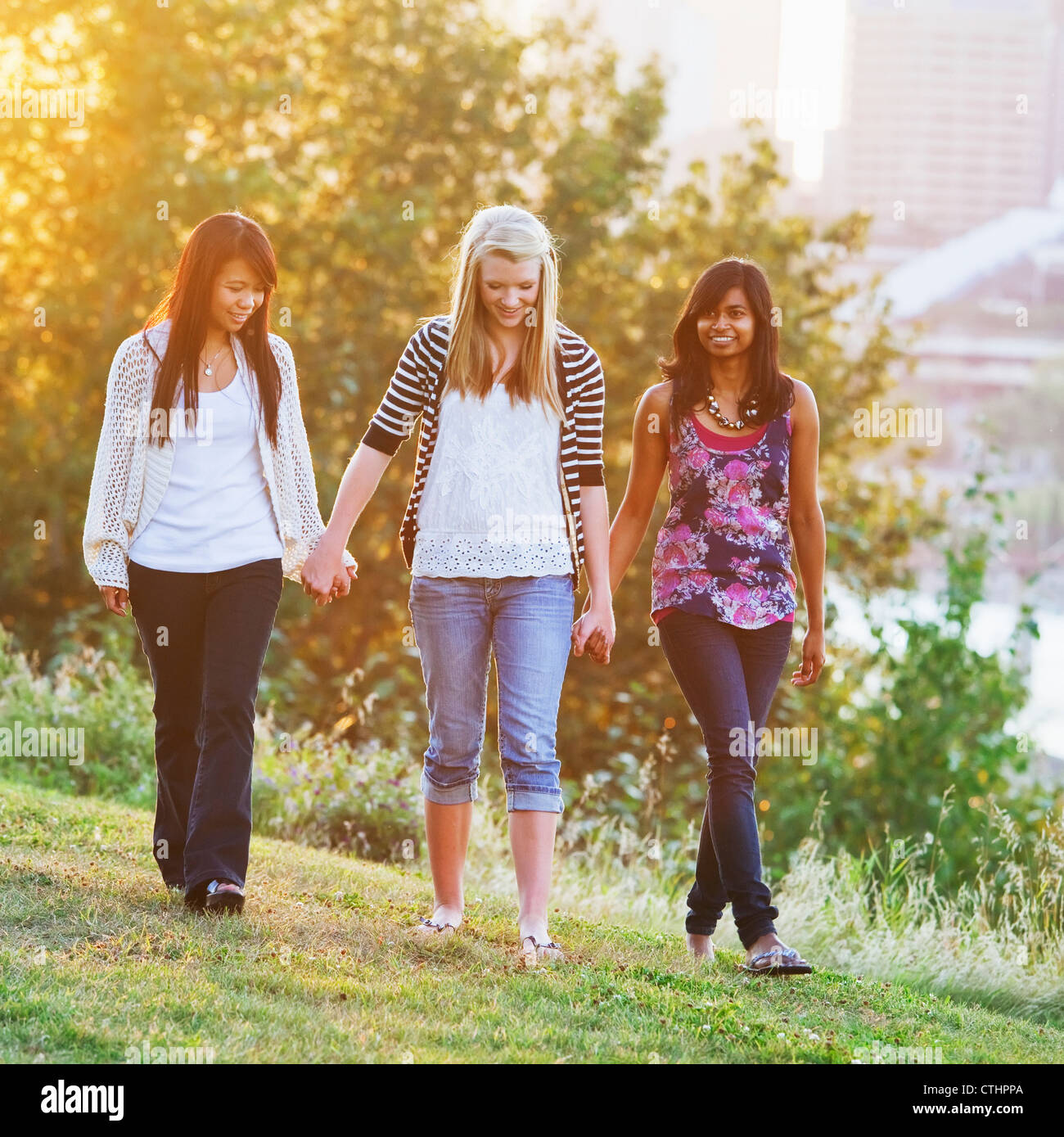 Friends Walking In A City Park At Dusk With The City Skyline In The Background; Edmonton, Alberta, Canada Stock Photo