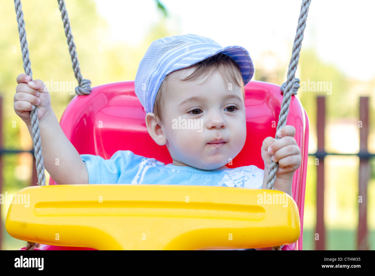 9-month old baby boy with blue hat in a swing outdoors Stock Photo