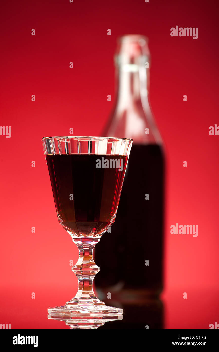glass of red wine or liqueur with bottle on red background Stock Photo