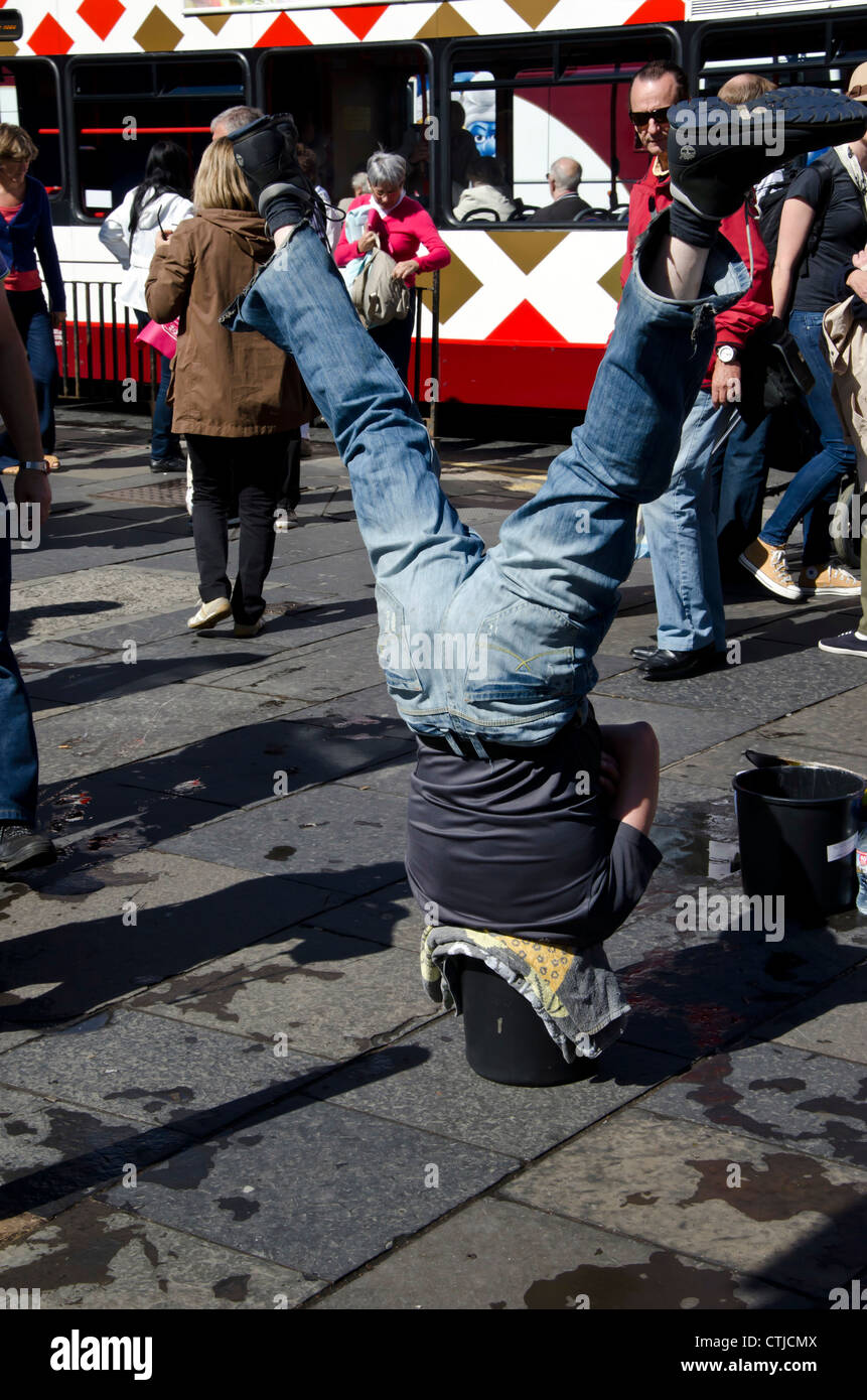 Man doing a head-stand with his head in a bucket in Princes Street, Edinburgh, Scotland. Stock Photo