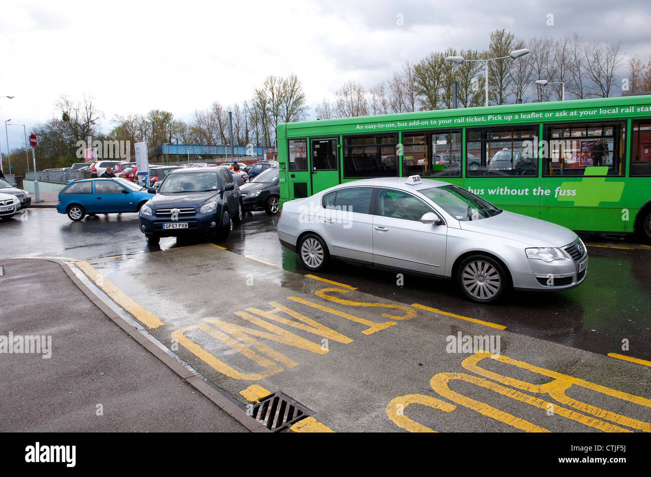 Taxi cabs and cars drive around a plusbus waiting at a bus stop outside Hatfield Railway Station, England. Stock Photo