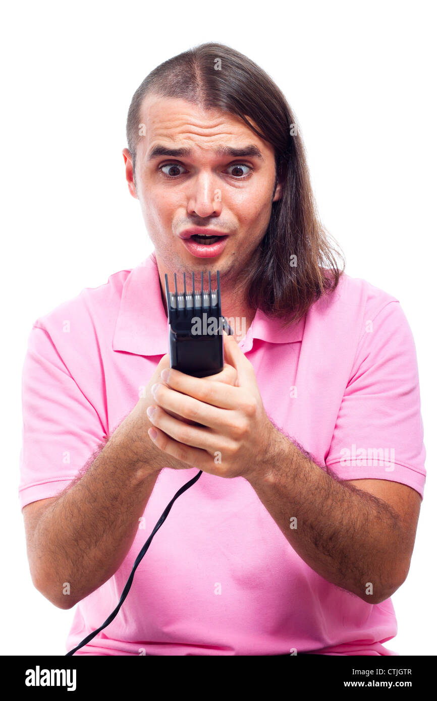 Unhappy shocked half bald young man holding hair trimmer, isolated on white background. Stock Photo