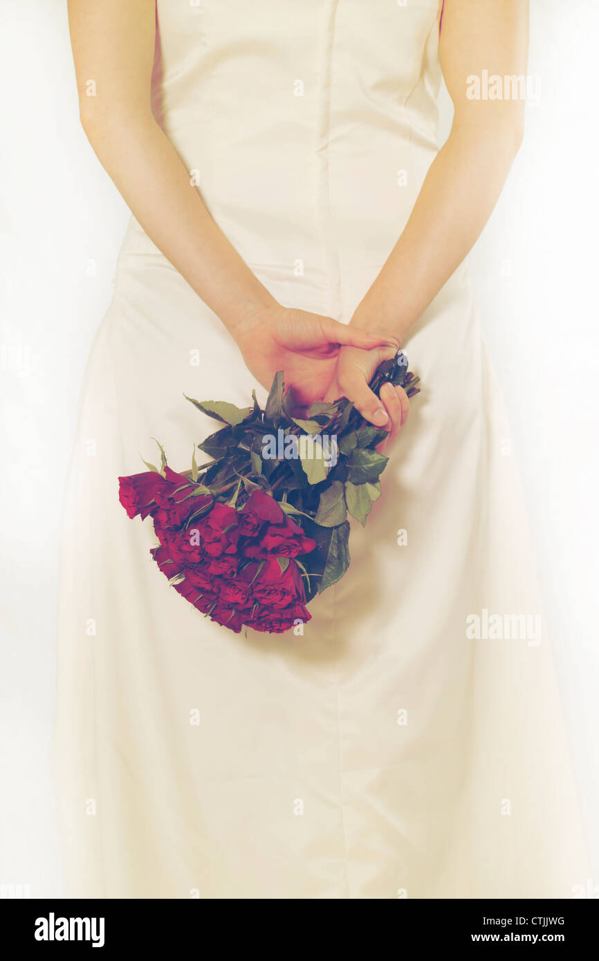 a woman in a white dress holding a bouquet of roses behind her back ...