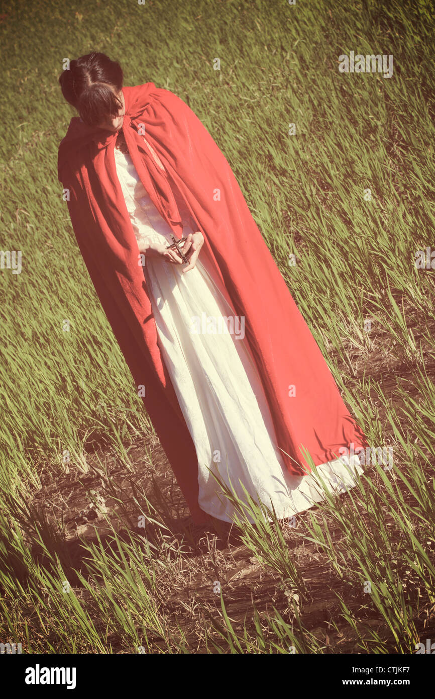 a woman in a red cloak holding a crucifix in her hands Stock Photo