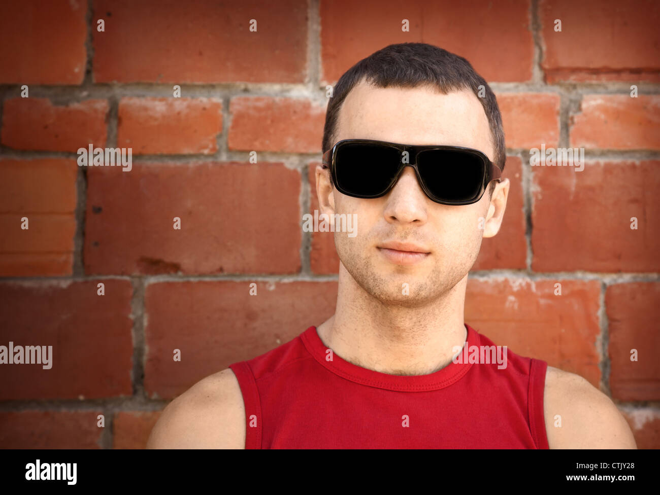 Closeup portrait of young man in black sunglasses over old brick wall Stock Photo