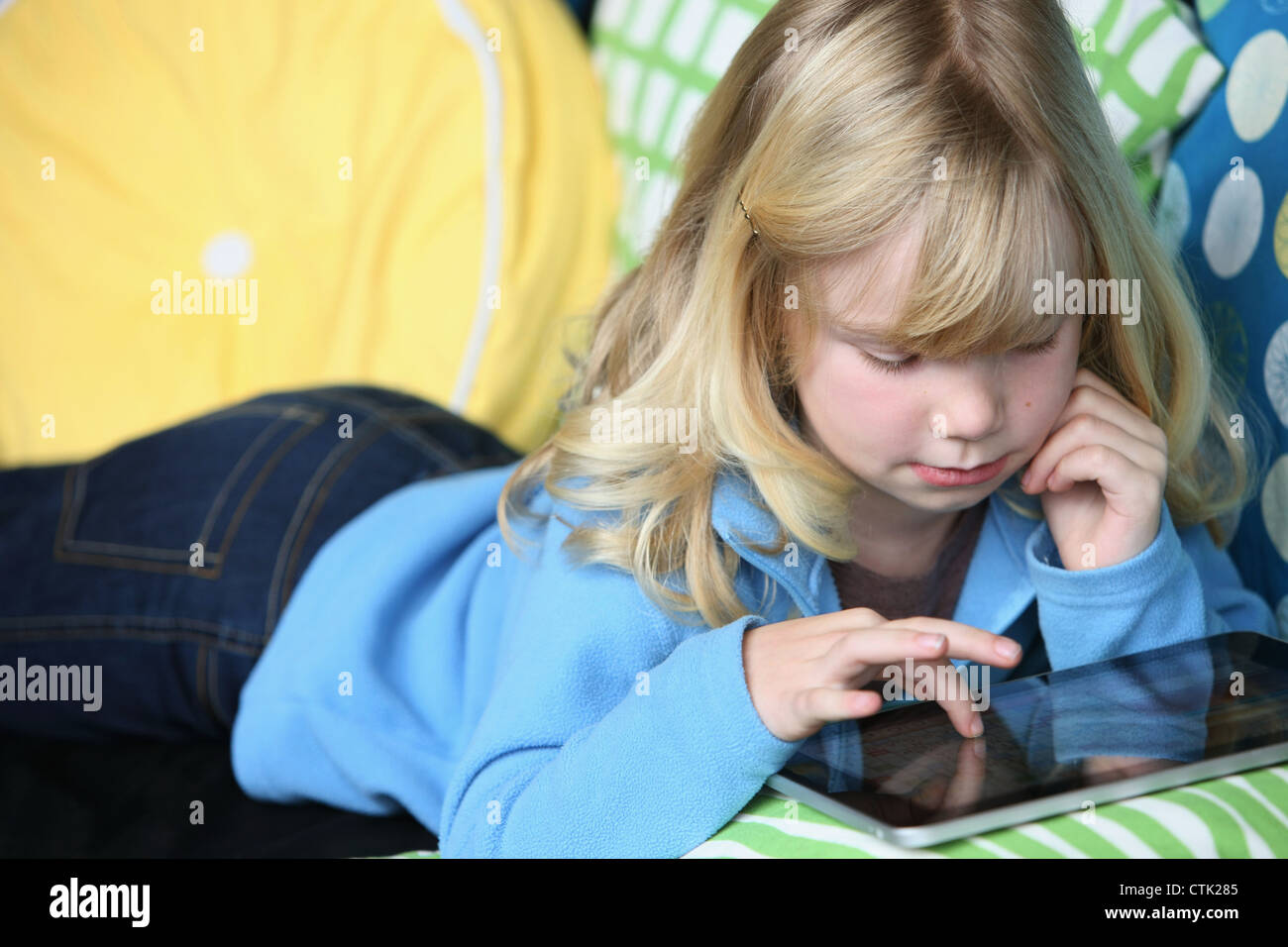 Young Girl Laying On A Couch Playing With An Electronic Notebook; Troutdale, Oregon, United States of America Stock Photo