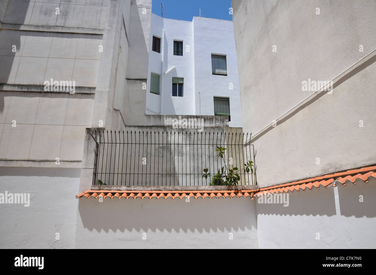 Blank white walls, wrought iron spiked fence, bleak street scene, hot midday sun, Seville Spain. Stock Photo