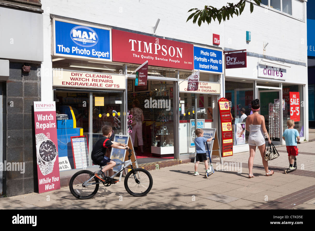 mother and children passing Timpson high street shop on sunny day Stock Photo