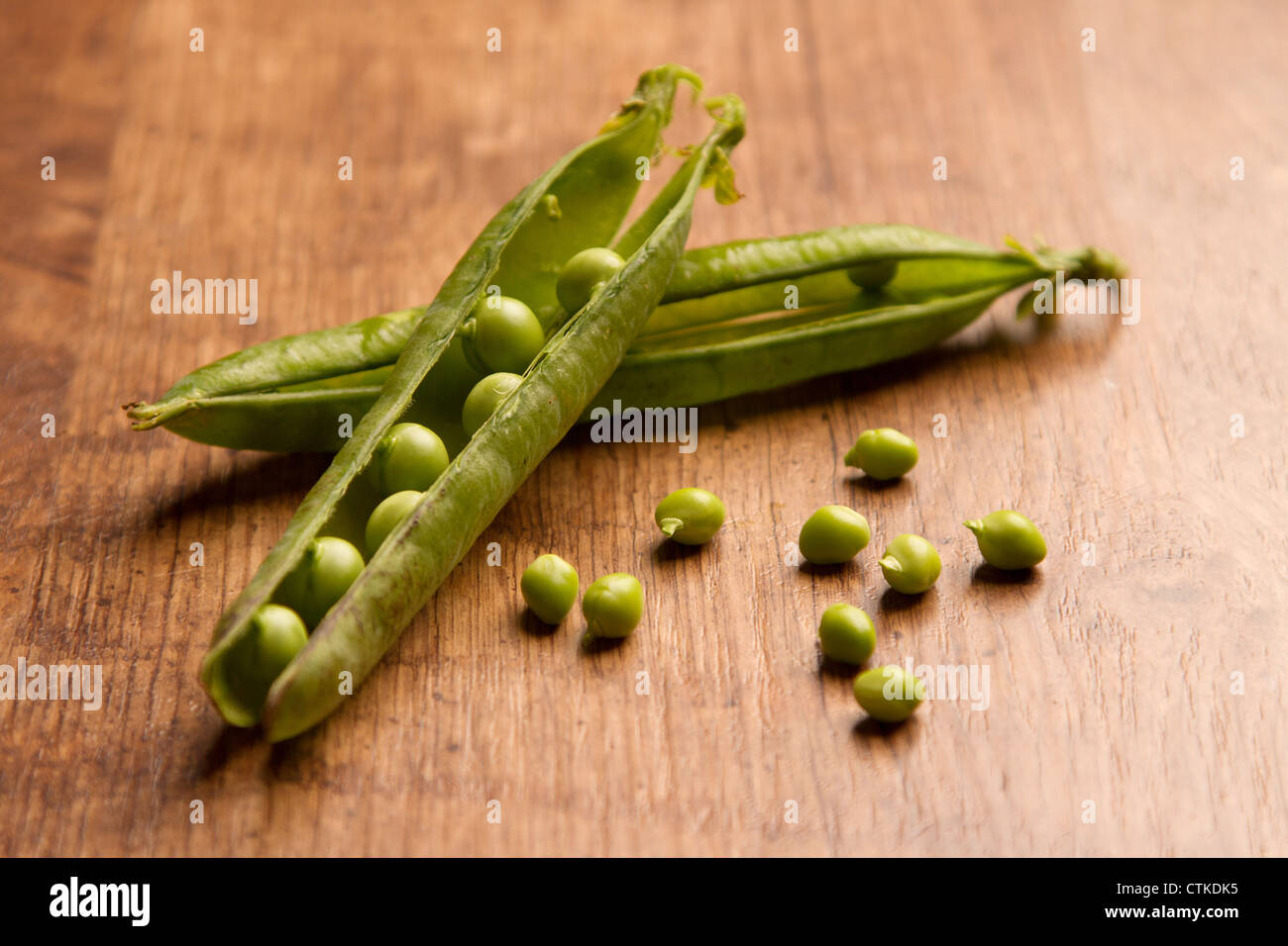 Two open pea pods with some loose peas, placed on a wooden background Stock Photo