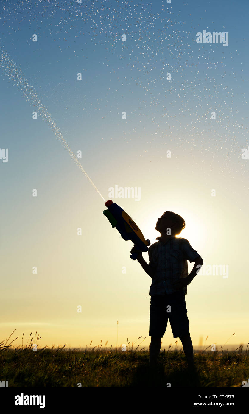 Boy shooting a water gun at sunset. Silhouette. UK Stock Photo