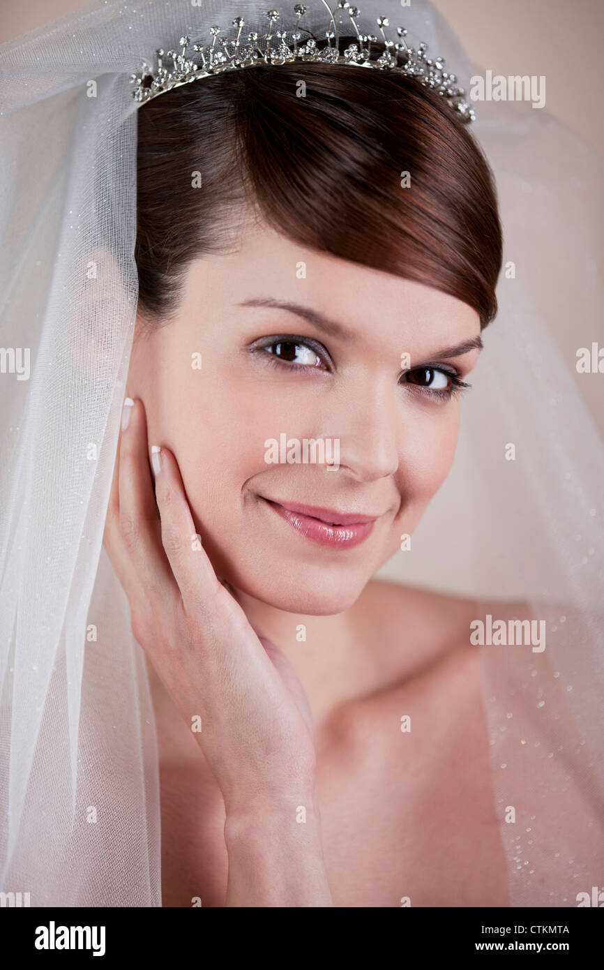 A young bride wearing a tiara and veil, hand on resting on her face