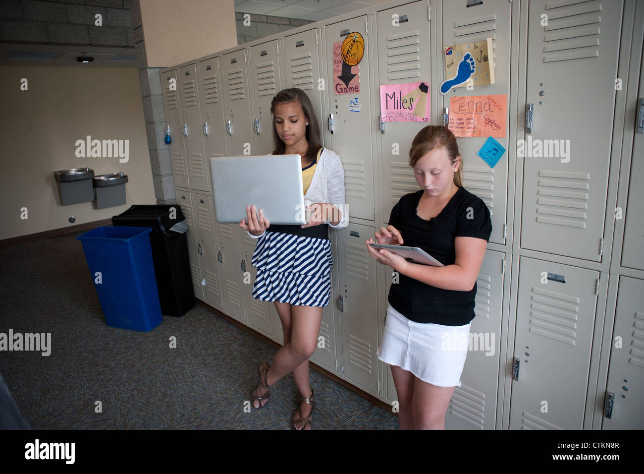 Teenage girls using ipad and laptop in middle school hallway. Stock Photo
