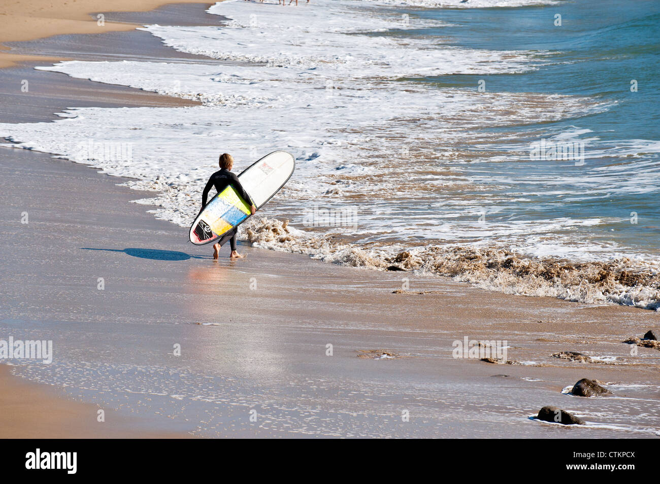 A surfer walking into of the sea at Alexandra Headland in Queensland Stock Photo