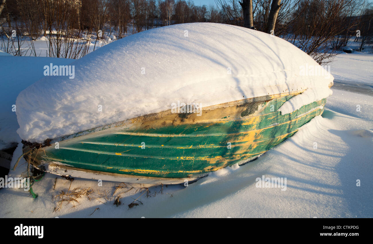 Snow covered old worn-out isolated fiberglass rowboat / skiff. beached at Winter , Finland Stock Photo
