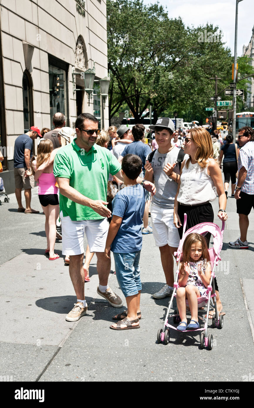 happy family with teenage son younger boy & small daughter in stroller pause on 5th Avenue sidewalk outside Bergdorf Goodman NY Stock Photo