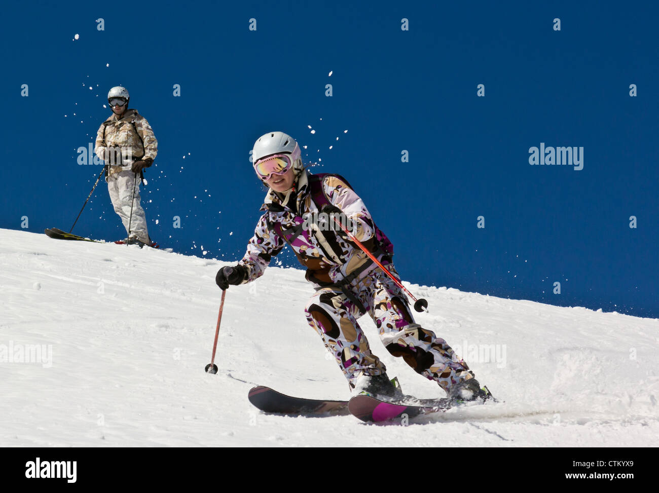 Woman skier descends the steep slope in deep snow in the sun. Stock Photo