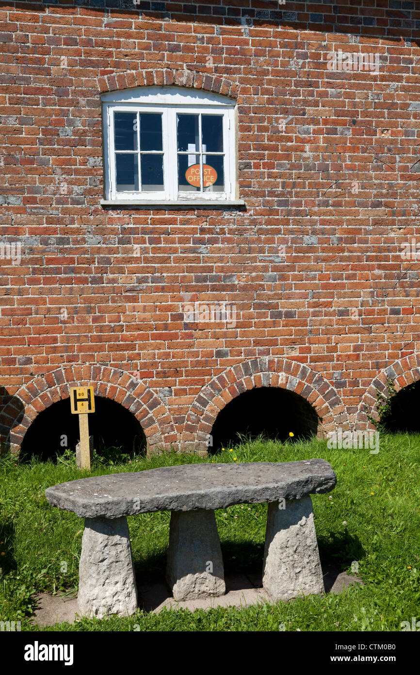 Unusual 'megalithic' style seat outside the arch-based wall of the Post Office, a former granary, in Briantspuddle, Dorset Stock Photo
