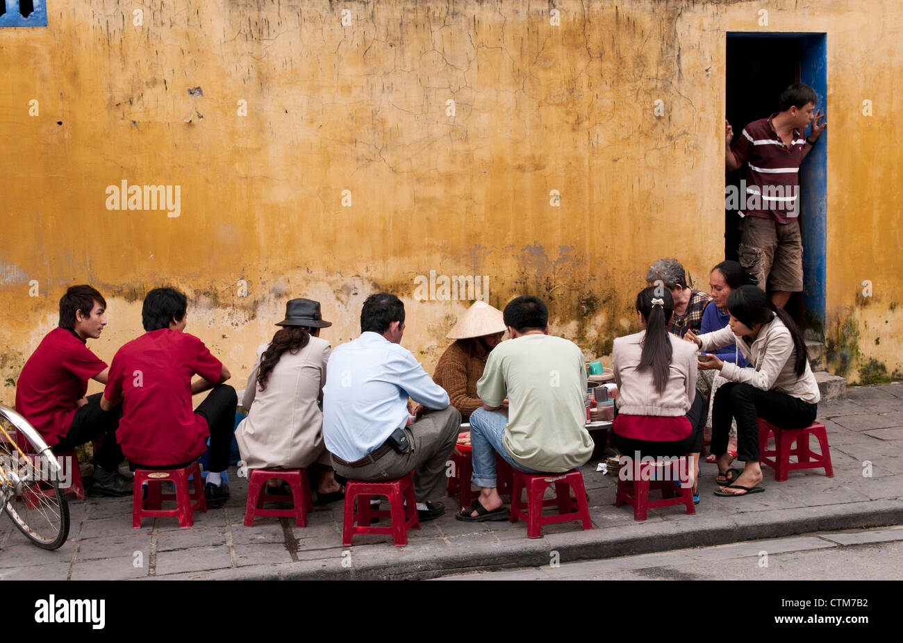 Customers sitting on low plastic stools eating at a street food noodle stall in Hoi An, Viet Nam Stock Photo
