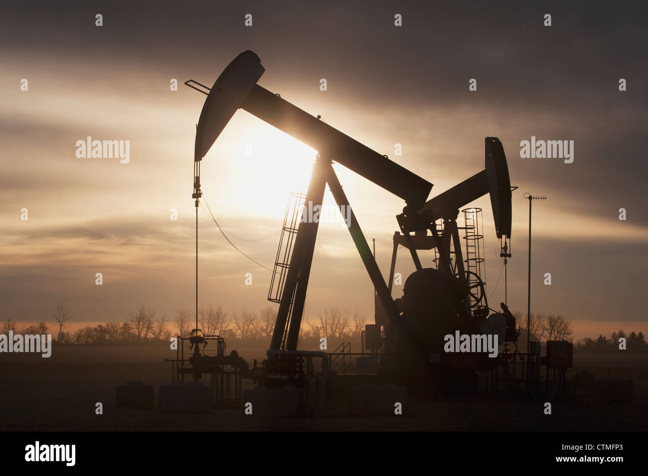 Silhouette Of Two Pump Jacks At Sunrise With Clouds; Alberta, Canada