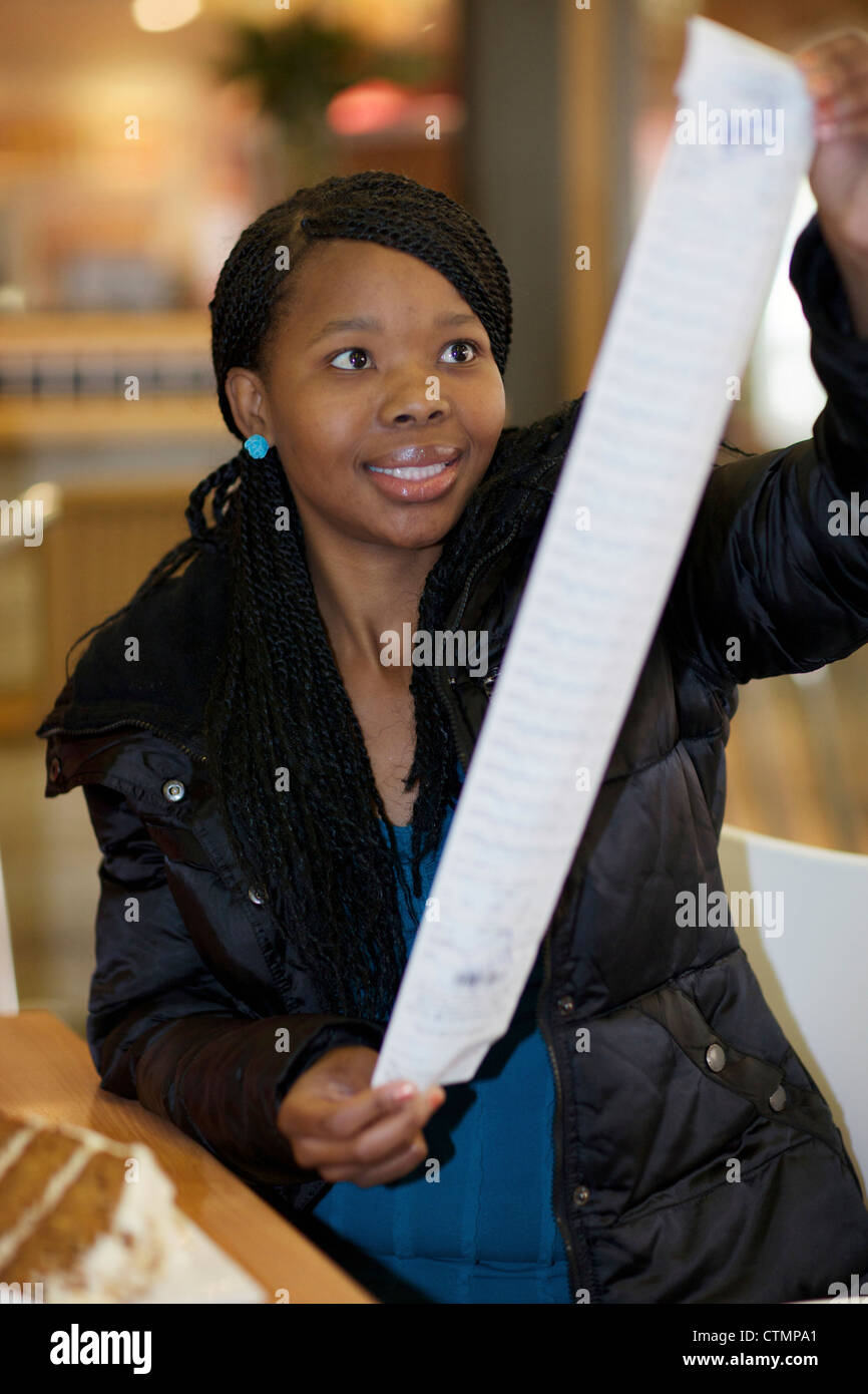 A young woman looking at her shopping bill while sitting at a coffee shop. Pietermaritzburg, KwaZulu-Natal, South Africa Stock Photo